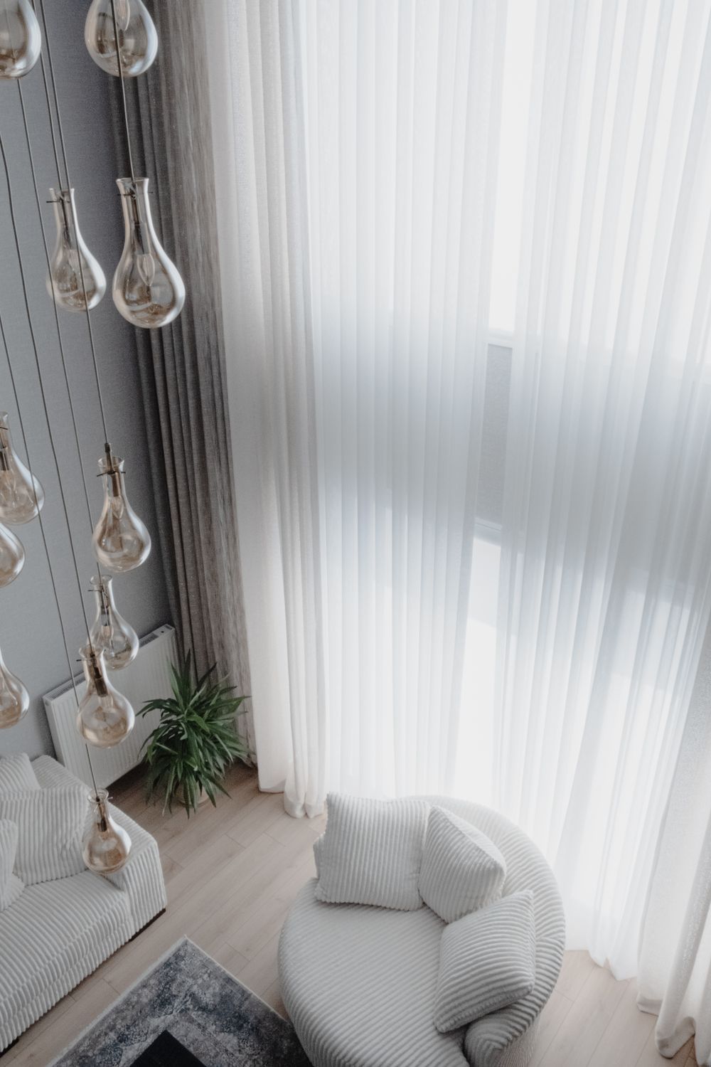 Finished residential lounge with full-height sheer curtains, grey drapery and glass pendant lighting